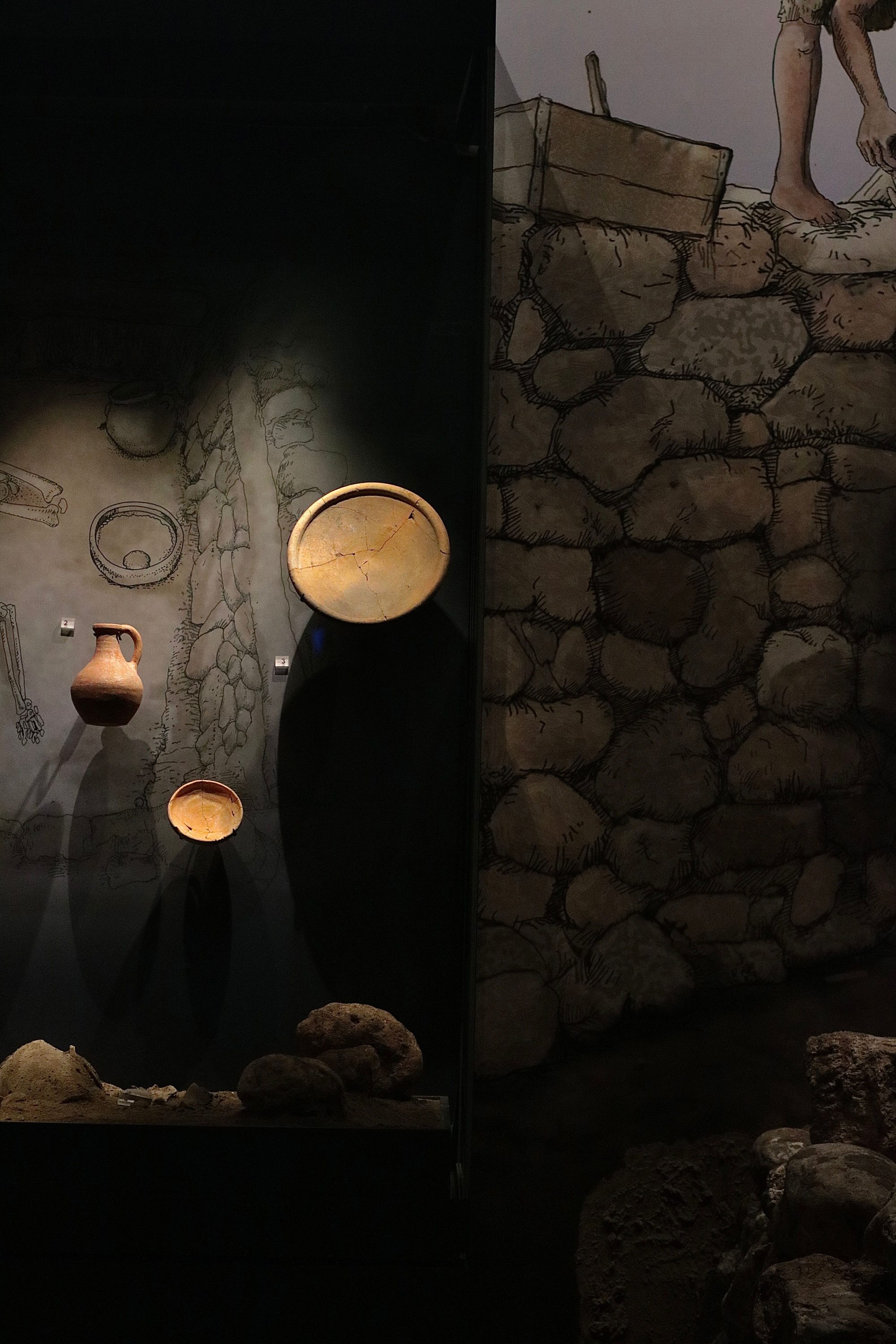 Showcase of ancient pottery and artifacts in a dimly lit museum setting.