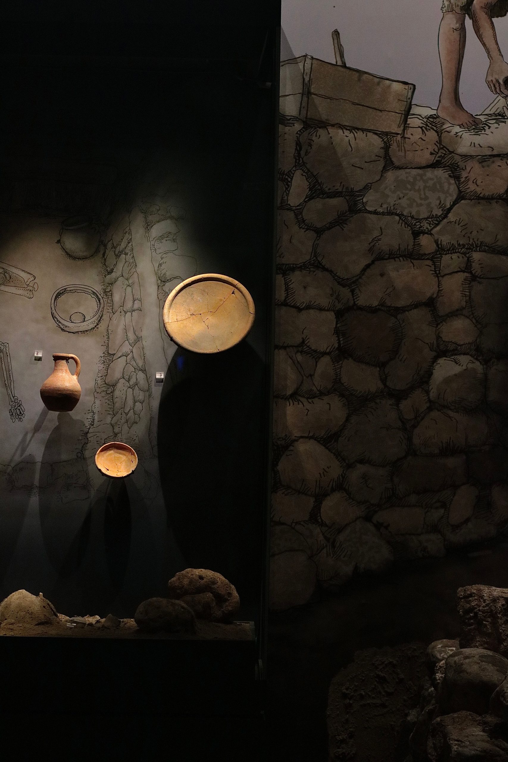 Showcase of ancient pottery and artifacts in a dimly lit museum setting.
