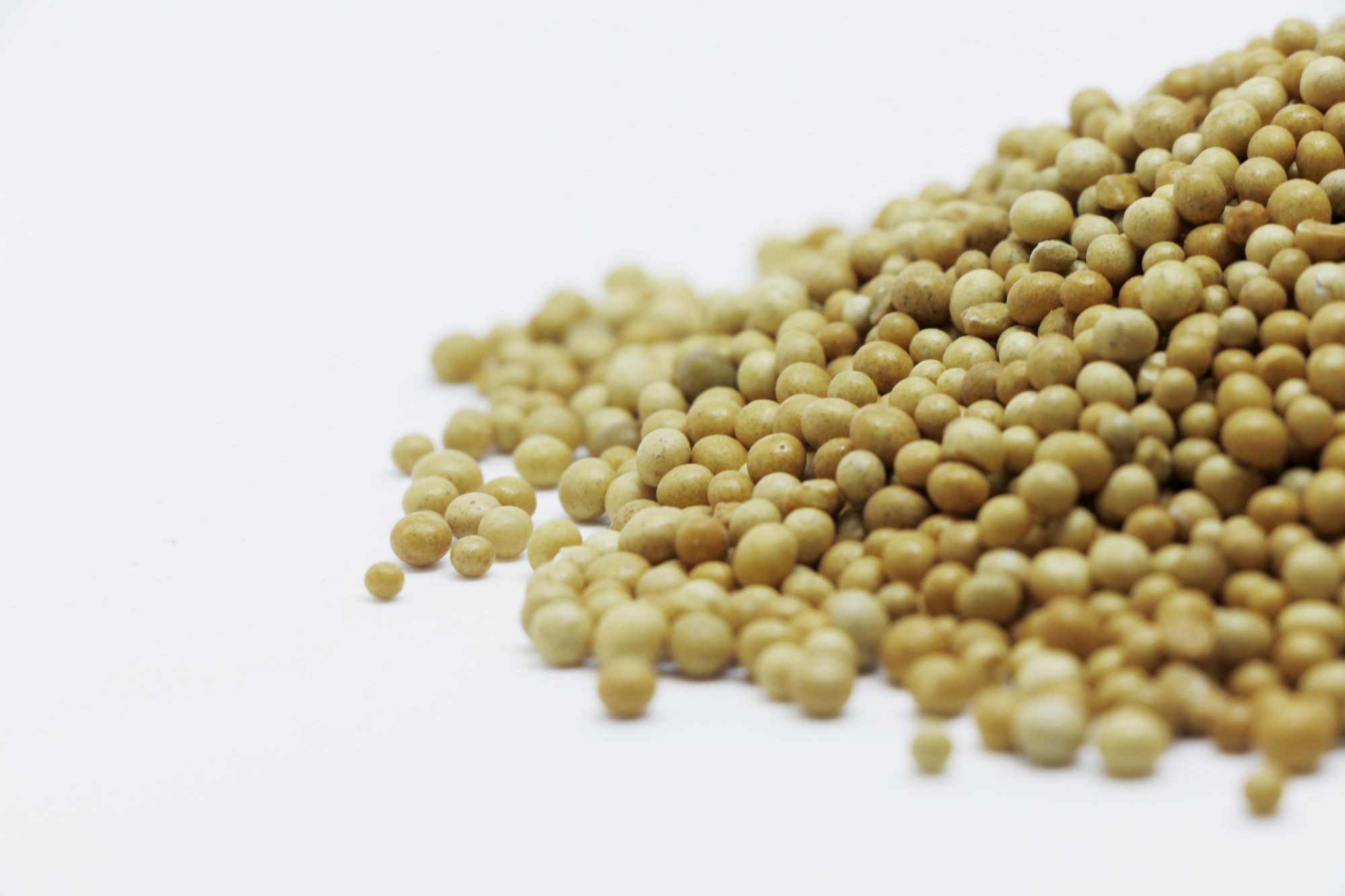 A close-up image showing a pile of brown mustard seeds on a white surface, highlighting their texture and color.