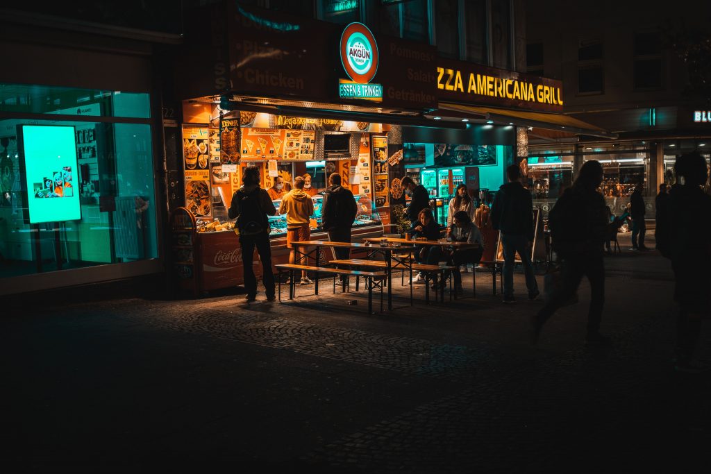 A lively street scene at night with people gathering around a pizza restaurant.