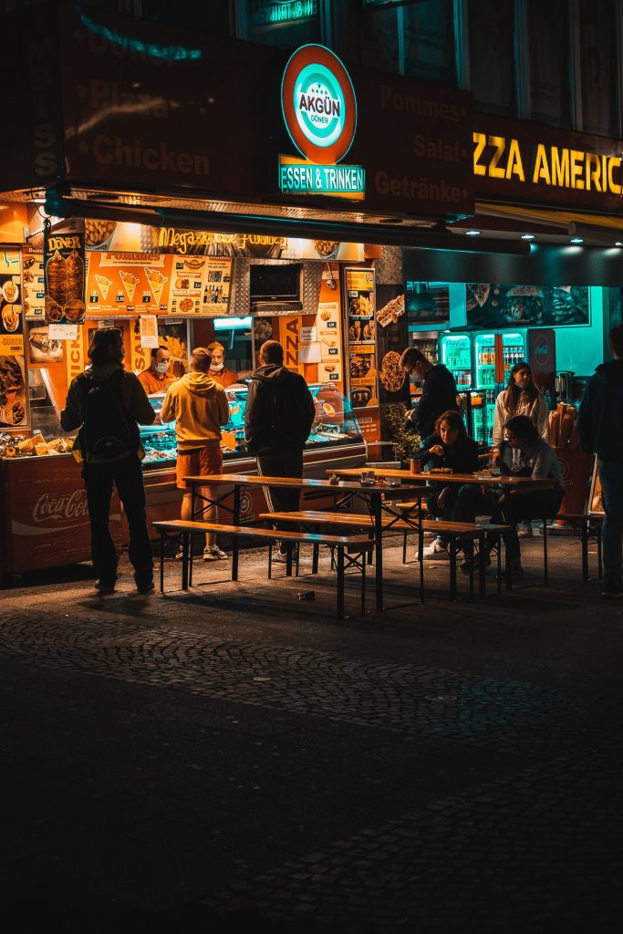 A lively street scene at night with people gathering around a pizza restaurant.