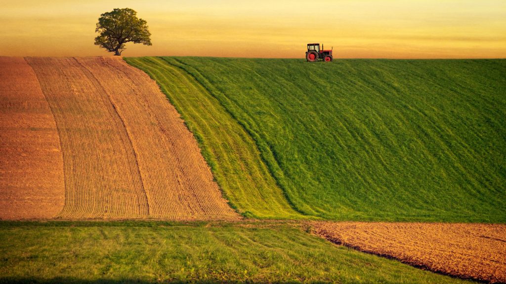 Lush green and brown fields with a lone tractor under a sunset sky.